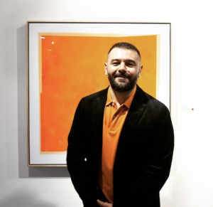 A photto of Artist Rick Carlino in front of one of his brightly-coloured epoxy-resin paintings on show at .M Contemporary, in Darlinghurst, Sydney.