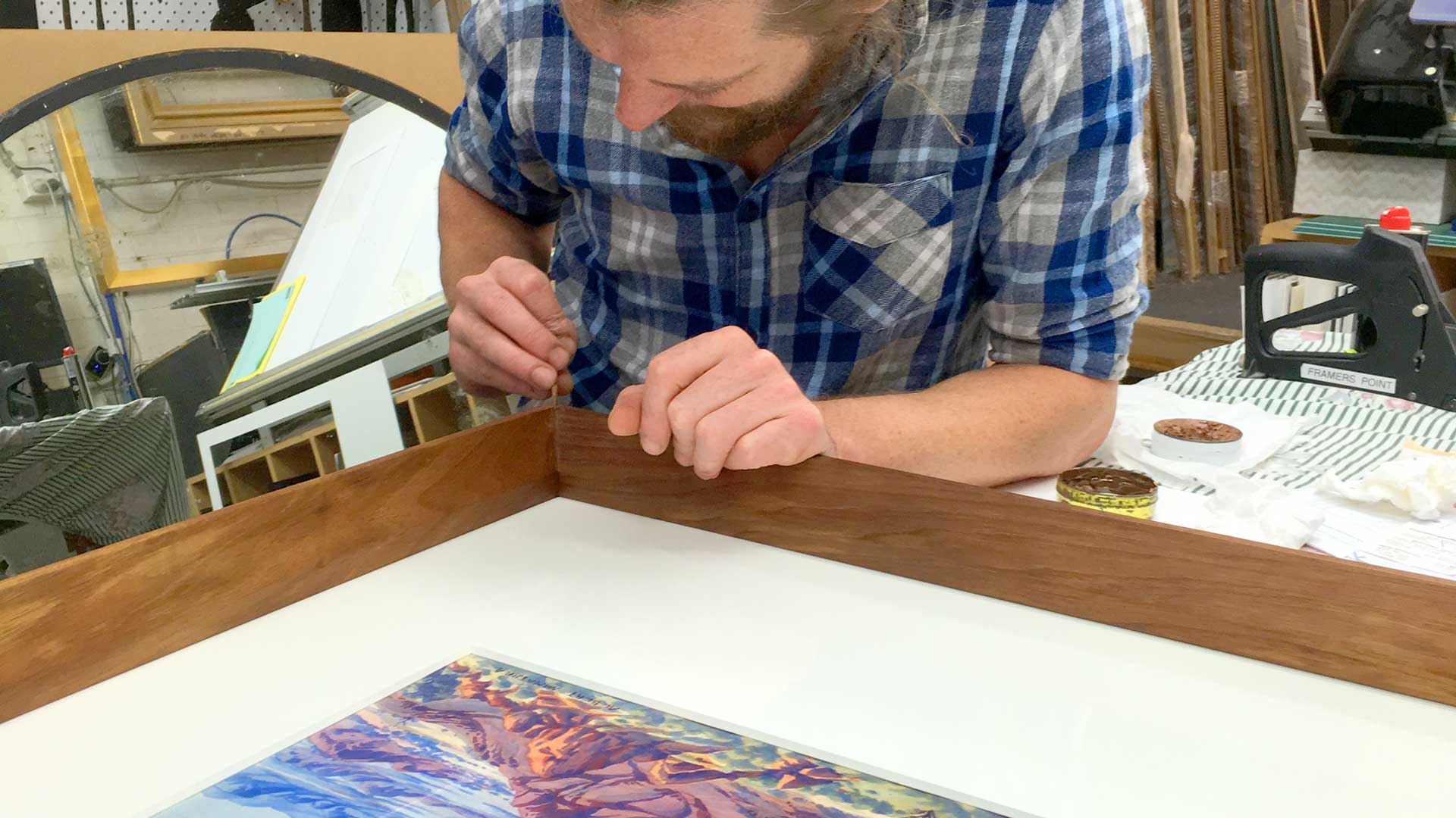 one of our workshop team members applying finishing touches to a hand-stained and waxed blackwood frame with artwork by Albert Namatjira